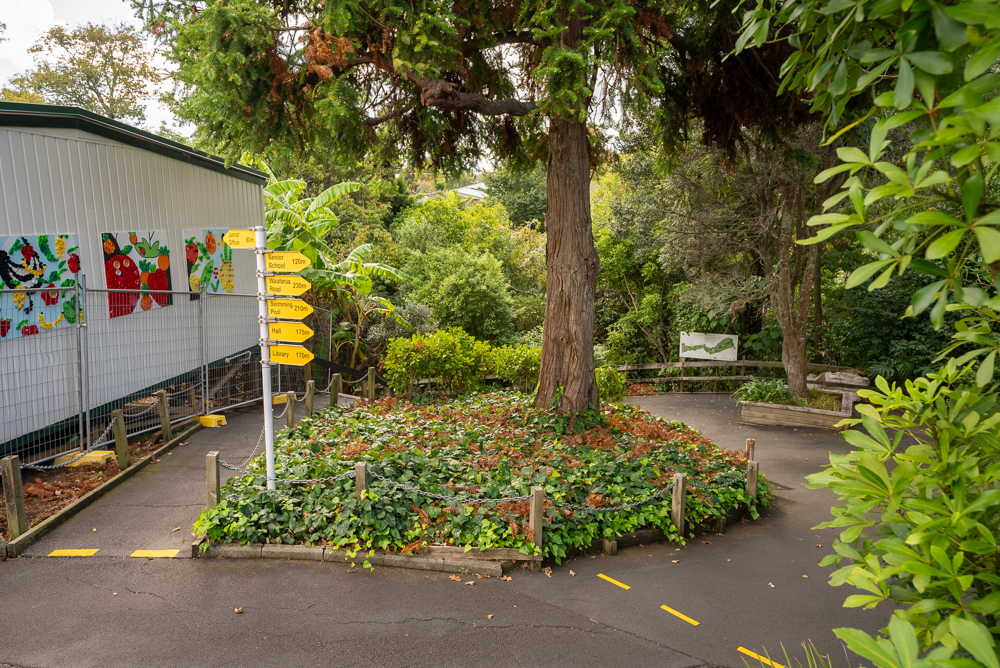 Exterior of schools with tress, mural on a classroom and signage on a pathway