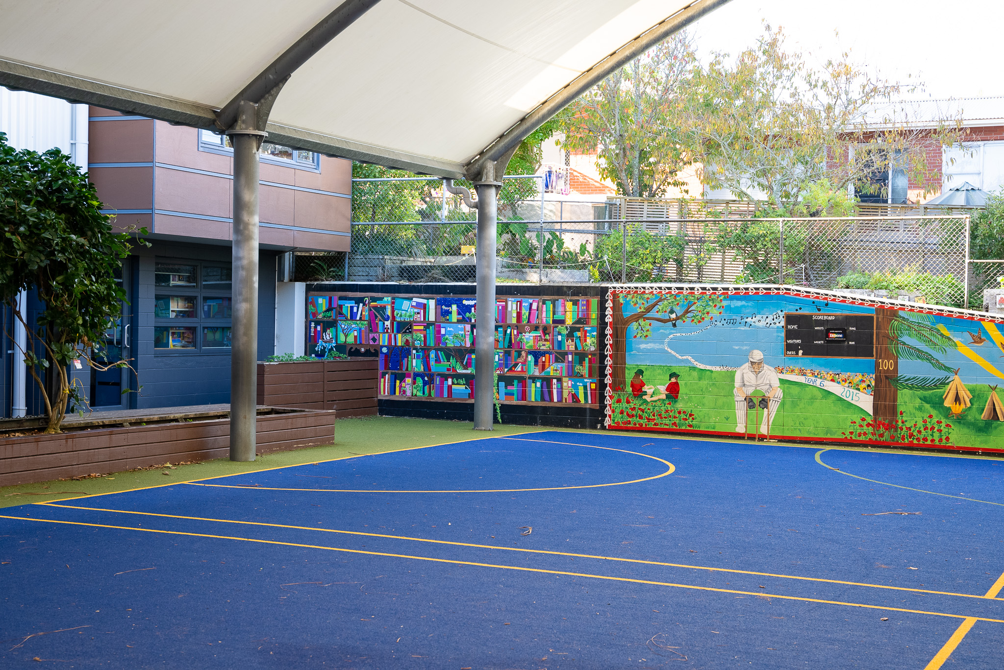 A blue turf basketball court with a mural at one end, covered with a roof but outside